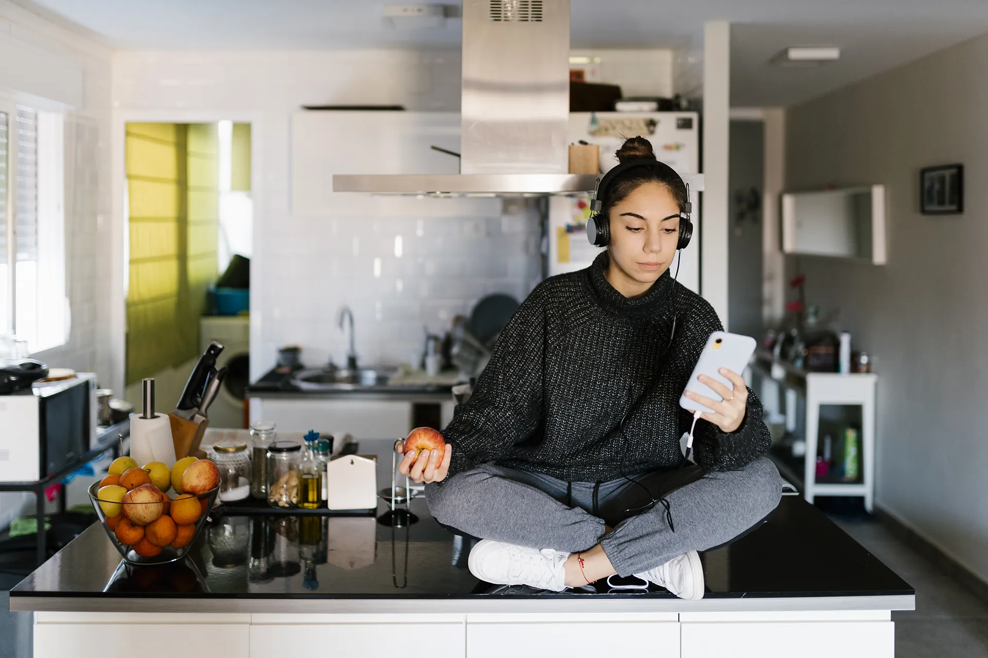 Teen sitting on kitchen counter holding apple on smart phone