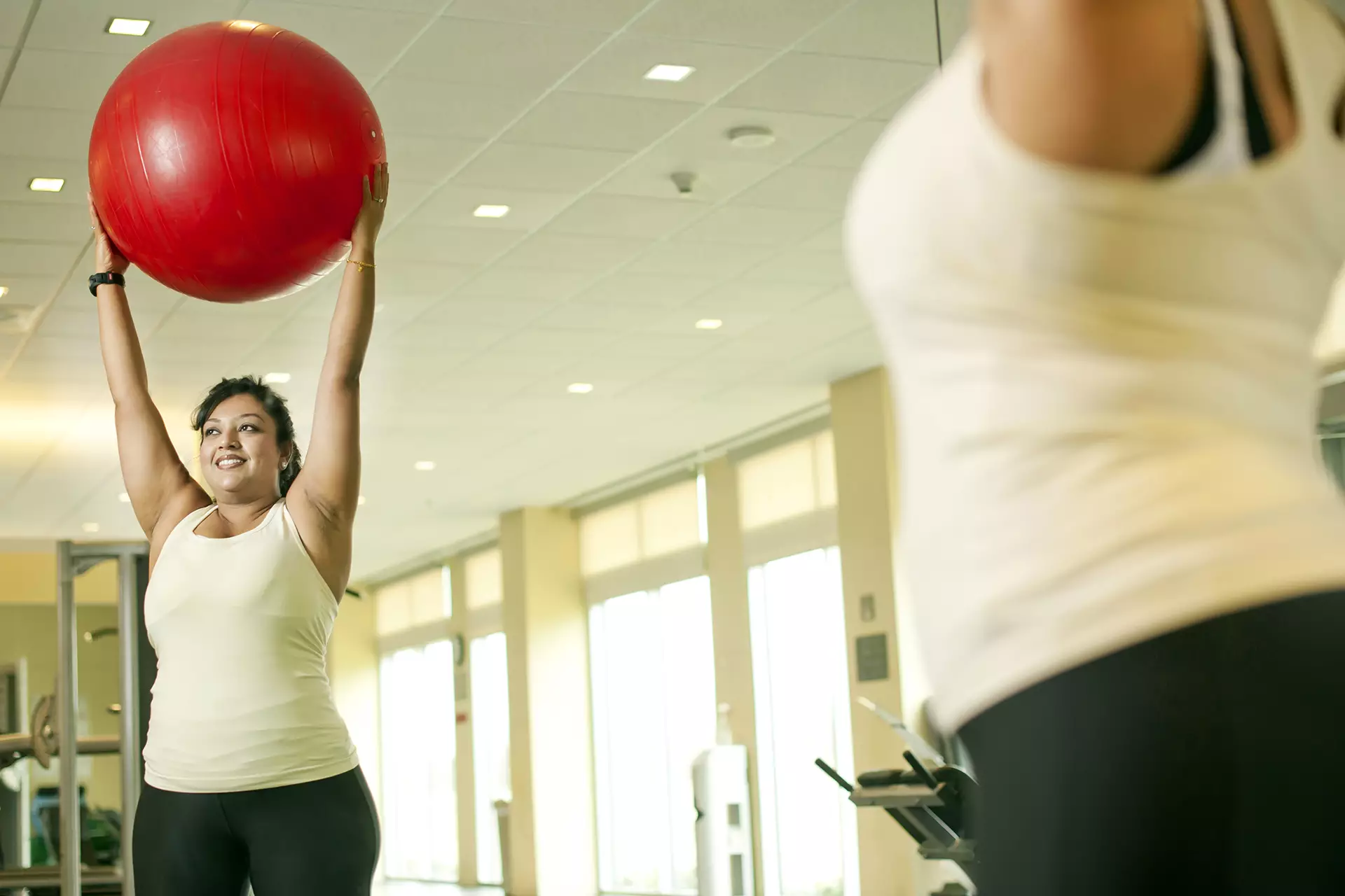 Woman in gym looking into mirror while holding exercise ball
