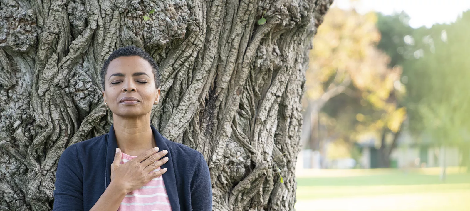 Woman sitting outside in front of tree meditating