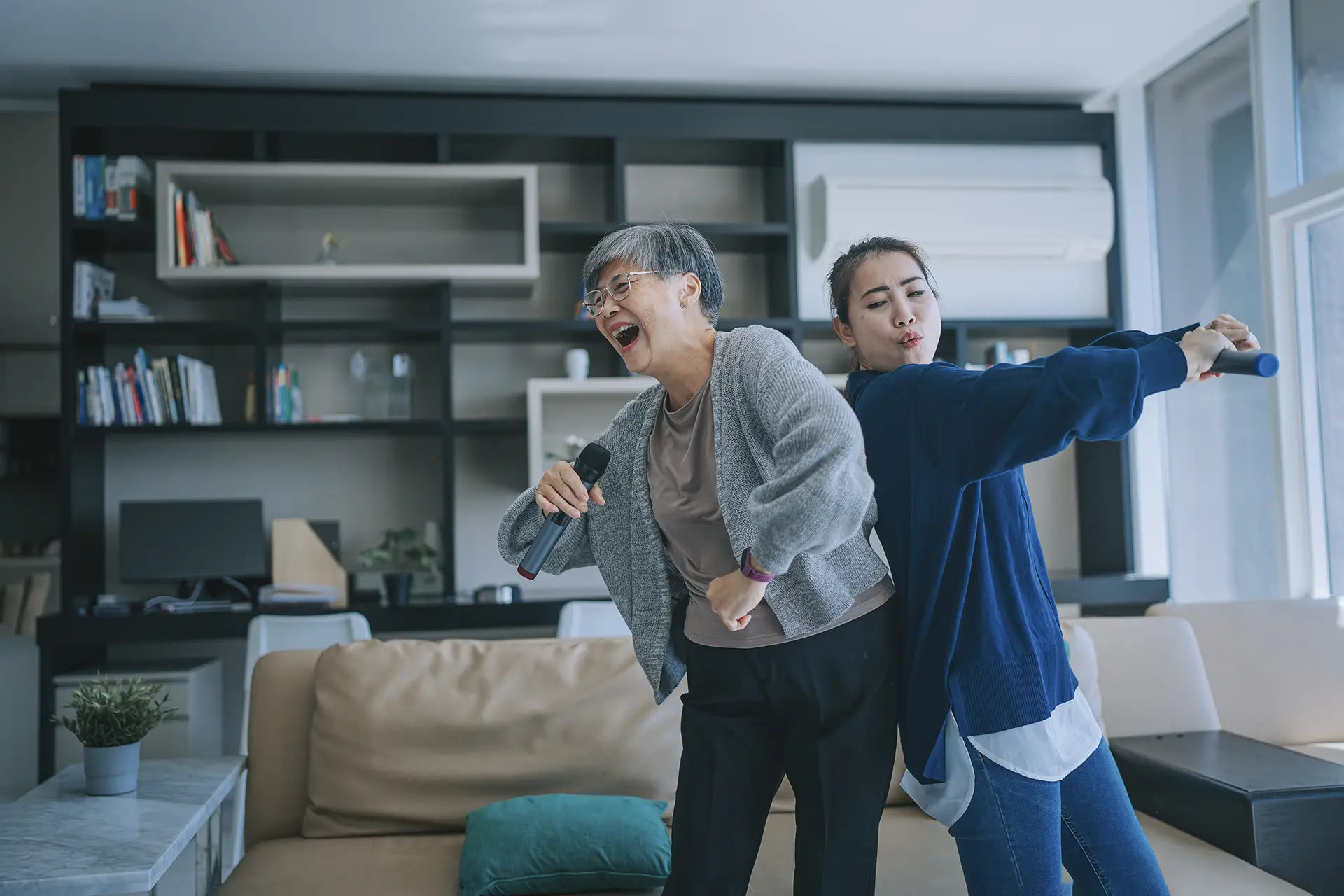 Mother and adult daughter singing karaoke at home